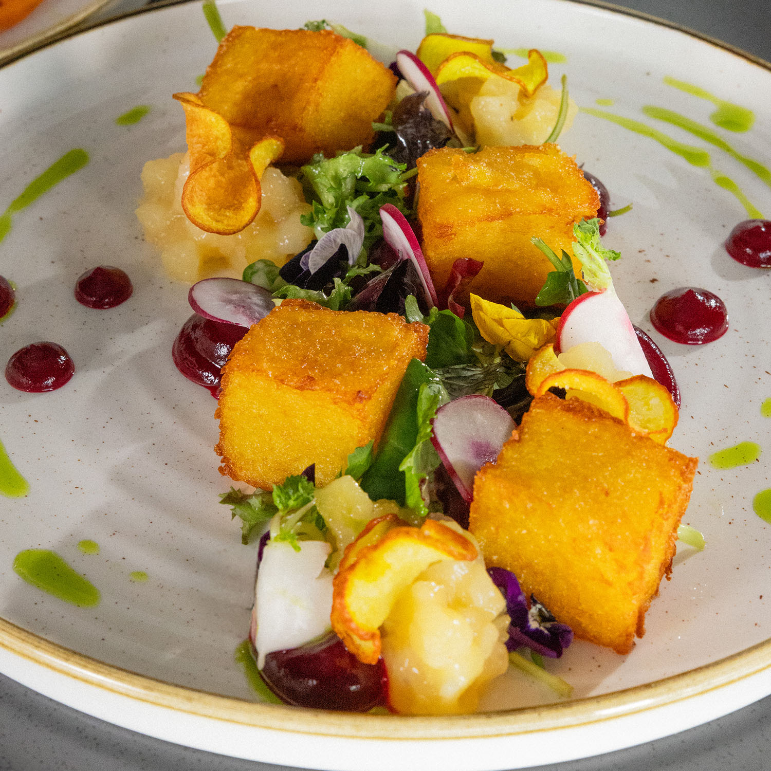 Kunstvoll angerichteter Teller mit buntem Gemüse und goldenen Würfeln, dekorativ beträufelt