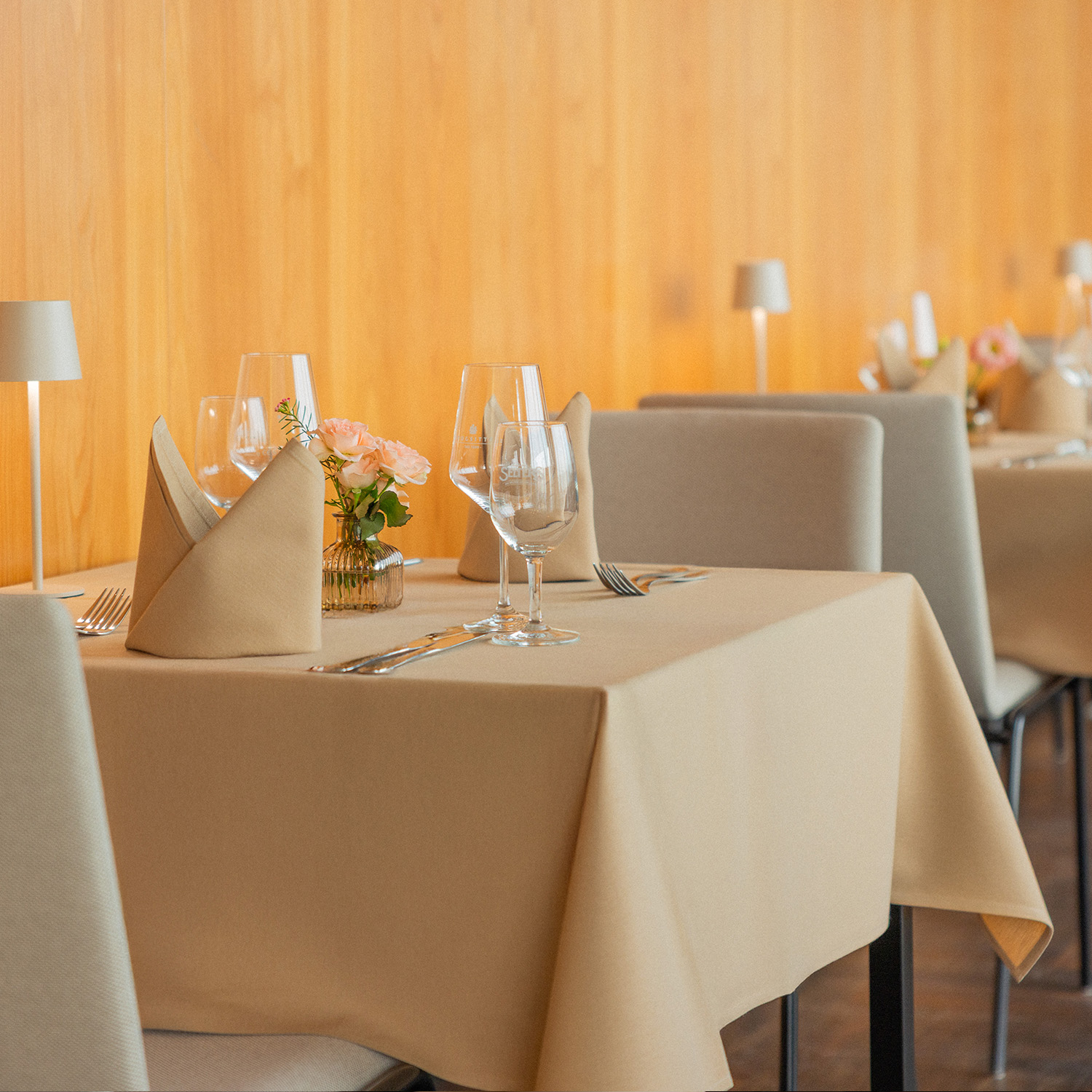 Elegant gedeckter Tisch mit beiger Tischdecke, Kerzen und Holzvertäfelung im Hintergrund