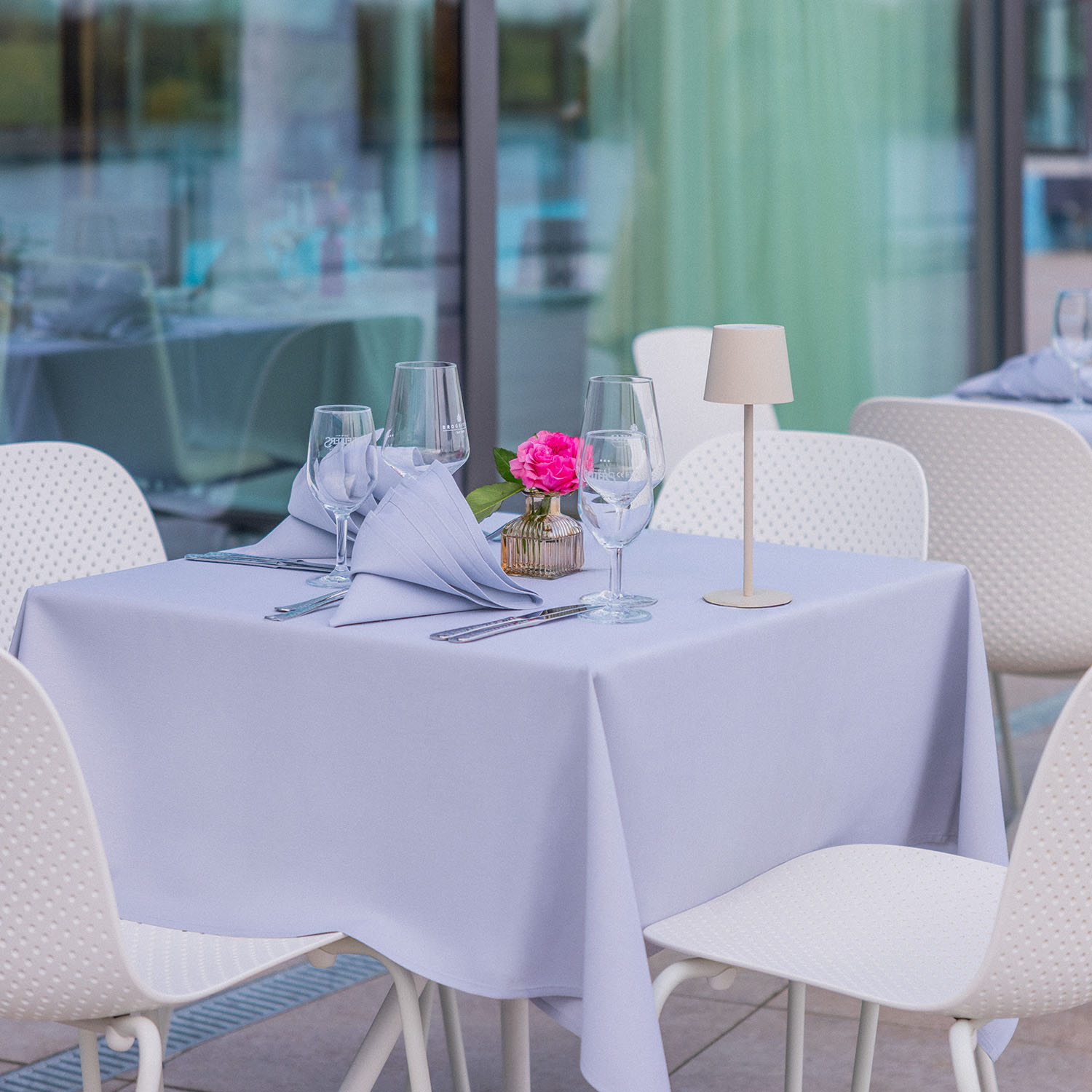 Runde Tische mit hellen Tischdecken und Blumenvase auf Terasse