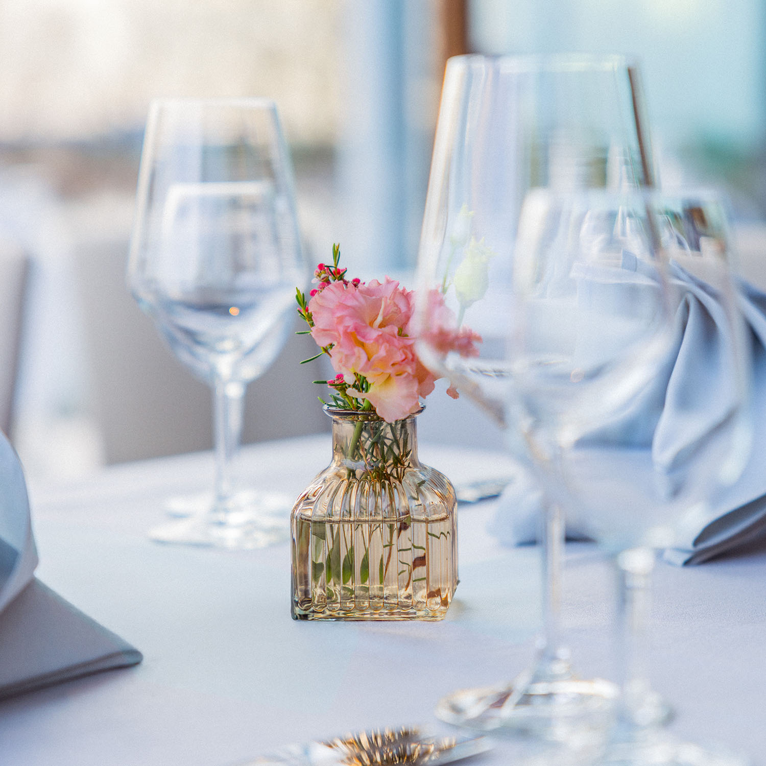 Gedeckter Tisch mit Weingläsern und kleiner Blumenvase in warmem Licht