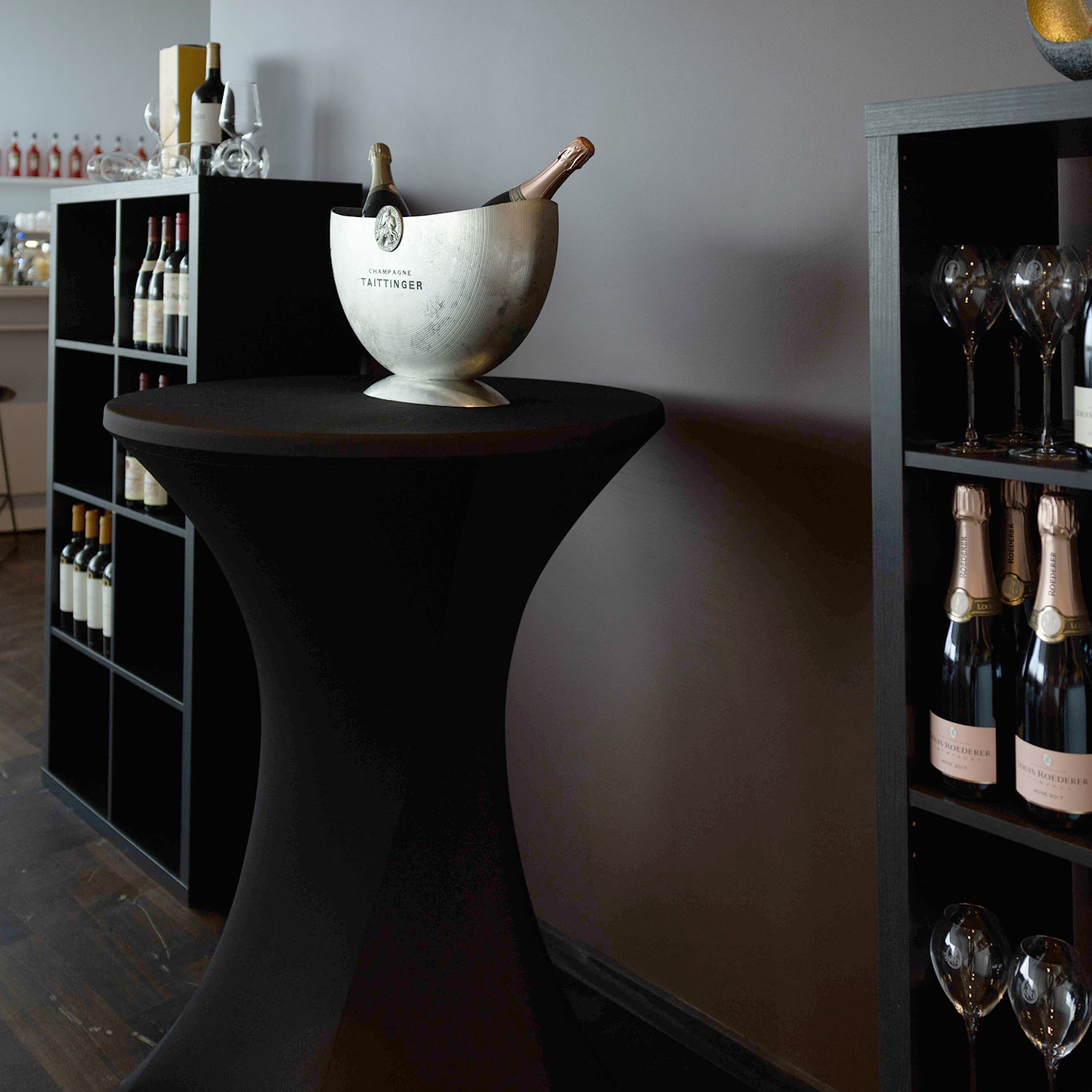 Stehtisch in Schwarz mit weißer Schale vor einer Bar mit Flaschenregal